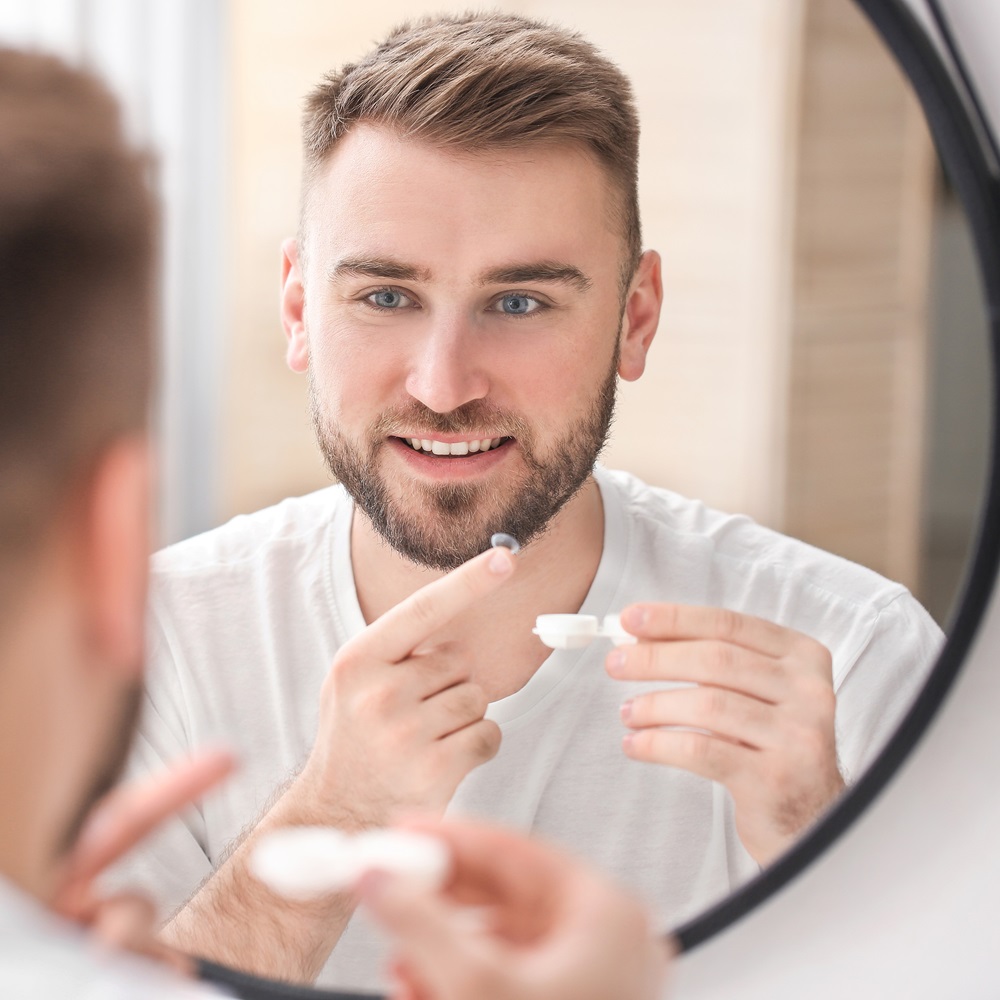 Young man putting in contact lenses near mirror